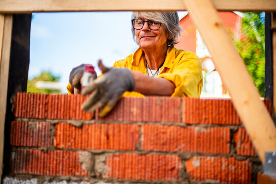 Short haired mature woman layering bricks while renovating house