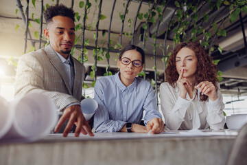 Skilled professionals discuss intricate project plans in a modern office surrounded by lush greenery