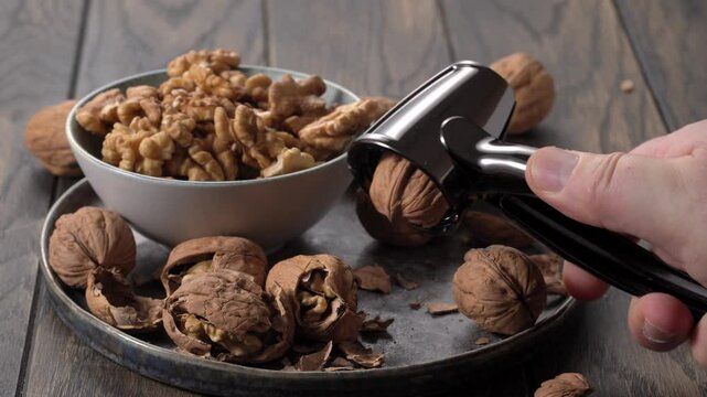 Hand holds black nutcracker over plate of walnuts on table.
