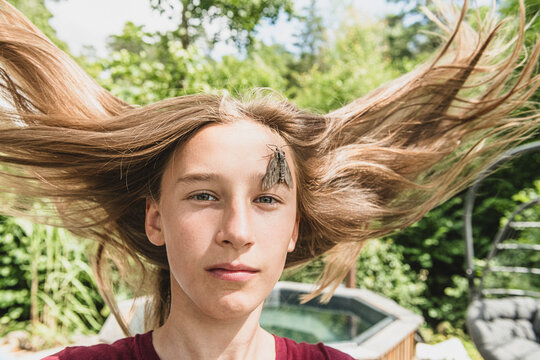 Portrait of girl with tousled hair and hawk moth sitting on face