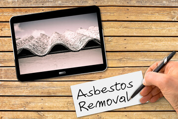 Hand writing Asbestos Removal text with a pencil on a white sheet above a wooden desk with a...