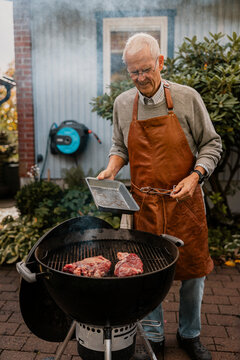 Senior man grilling meat on barbecue in back yard