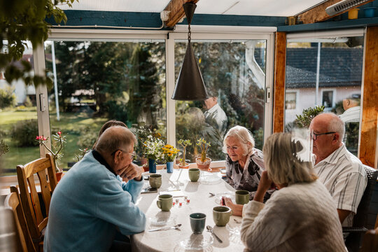 High angle view of male and female family friends playing dice game while sitting near table at patio of house
