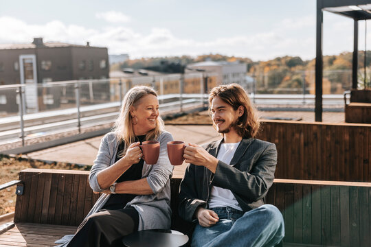 Smiling male and female business professionals clinking coffee mug while sitting on bench at office park