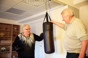 Elderly man helping female friend punching on bag while training in rehabilitation center