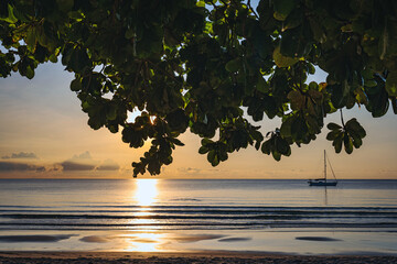 朝焼けの海辺とヨットのシルエット