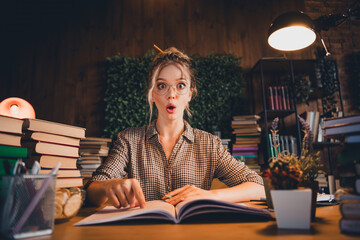 Surprised student studying late at night in casual checkered shirt with books and natural light...