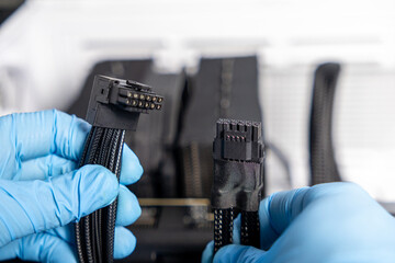 Close-up of gloved hands holding two different GPU power connectors with visible pins during computer hardware installation or upgrade
