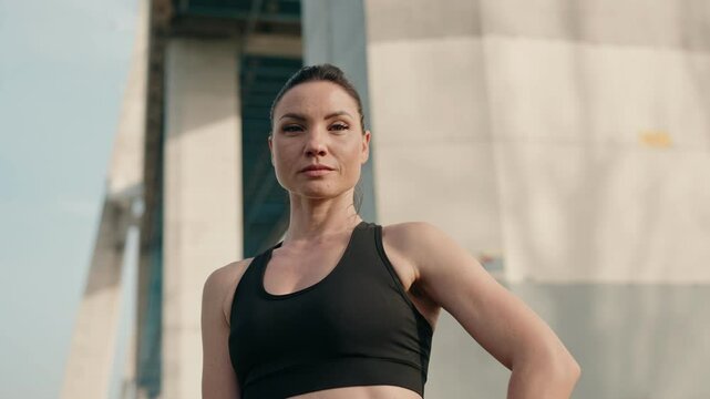 Determined woman in her 40s dressed in athletic wear, exuding confidence in an urban outdoor setting, standing and looking at camera