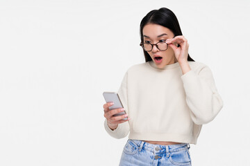 Portrait of amazed shocked surprised young Asian woman holding and using smartphone, looking at...