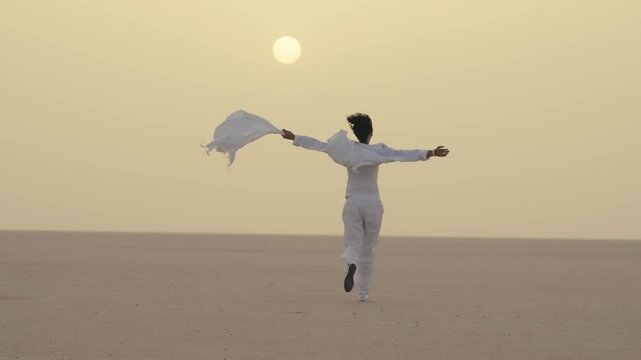 Woman running gracefully in the vast Sahara Desert under the golden sunrise, holding out a flowing scarf while embracing the peaceful and expansive beauty of the scenery