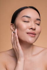 Vertical shot of young Asian woman girl with clean fresh skin on beige background touching her face...