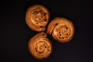 Puff pastry snail with maple syrup and raisins on a black background, top view