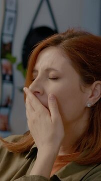 Vertical Screen: Woman sits at her home office desk, visibly tired and yawning as she tries to focus on her work. She battles fatigue and boredom despite her efforts to stay engaged.