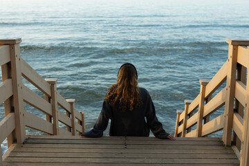 Girl with headphones sitting on the threshold overlooking the beautiful sea