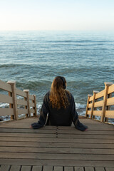 Young girl with headphones sitting on the seashore and listening to music