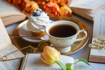 Cup of tea and cake on the table with beautiful spring flowers tulips.