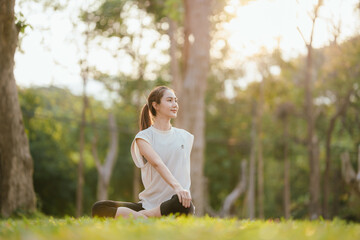 Young Asian woman practicing yoga in a quiet park, gracefully in a relaxed pose, relaxing and...