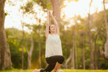 Young Asian woman practicing yoga in a quiet park, gracefully in a relaxed pose, relaxing and...
