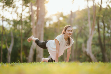 Young Asian woman practicing yoga in a quiet park, gracefully in a relaxed pose, relaxing and...