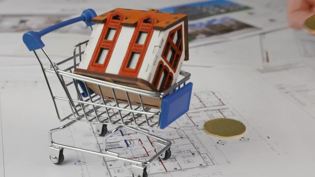 A house model in a shopping cart. Concept of paying for real estate with bitcoins. High quality 4k footage