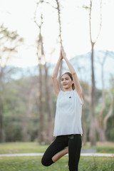 Young Asian woman practicing yoga in a quiet park, gracefully in a relaxed pose, relaxing and...