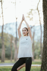 Young Asian woman practicing yoga in a quiet park, gracefully in a relaxed pose, relaxing and...