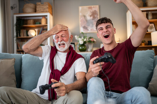 Grandson and grandfather playing videogames on sofa at home: generation gap