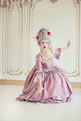 Fototapeta premium Young woman dressed in an elegant pink baroque gown, seated gracefully in a vintage interior setting with ornate wall designs