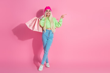 Young woman in trendy casual outfit holding shopping bags against a vibrant pink background