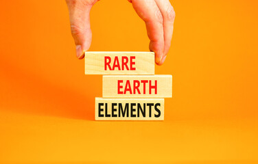 Rare earth elements symbol. Concept words Rare earth elements on beautiful wooden block. Businessman's hand. Beautiful orange background. Business and rare earth elements concept. Copy space.