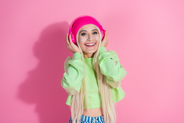 Cheerful young woman with pink headphones, smiling in a stylish green sweatshirt against a vibrant pink background