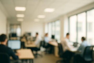 Blurred office environment depicts employees concentrating on their computer screens, showcasing a busy workday in a modern workspace with natural light