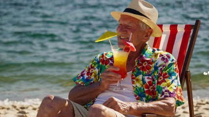 Elderly man wearing hawaiian shirt and hat relaxing on beach chair, holding colorful cocktail and smiling, enjoying retirement by the ocean