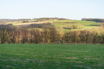 Fototapeta premium Panoramic photo of countryside in spring with blue sky and clouds on the horizon. Sawmill car near forest plantation. German landscape concept