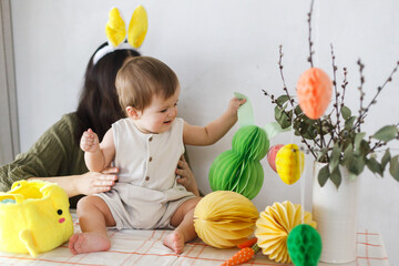 Happy Easter! Cute baby bunny and happy mother together playing with colorful easter paper eggs,...
