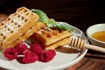 Juicy waffles drizzled with honey, topped with fresh raspberries and basil leaves, served on a...