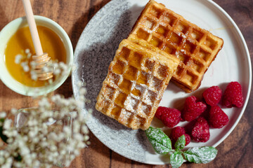 Juicy waffles drizzled with honey, topped with fresh raspberries and basil leaves, served on a...