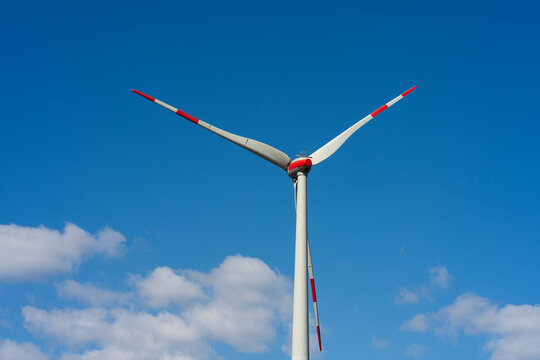 A lone wind turbine against a blue sky and white clouds. Green energy concept - Powered by Adobe