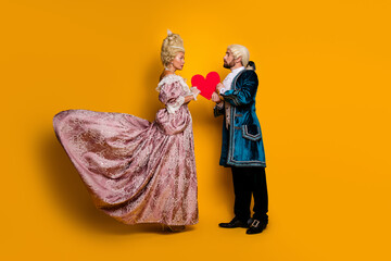 A couple dressed in retro aristocratic costumes sharing a romantic moment with a heart prop on a...
