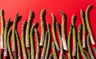 Green asparagus on red background. Vegetable food top view. Sprouts stems.