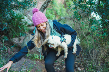 Hiker carrying her small white dog while descending a rocky trail in a nature preserve