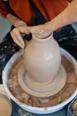 Close-up of a potter's hands making a ceramic vase on a potter's wheel. Vertical photo. 