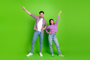 Obraz premium Young couple striking playful poses pointing upward on a green background, showcasing joy, friendship, and a fun casual lifestyle
