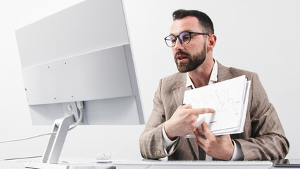 A businessman in a business suit holds a video conference at his computer and reprimands a team of...