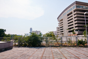 Urban landscape with a modern multi-story building, chain-link fence, and paved area.