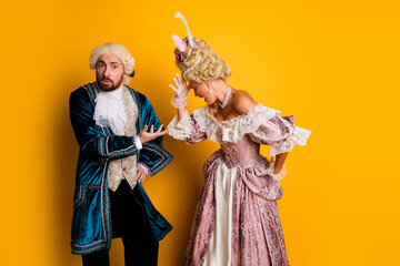 Elegant couple in historical costumes posing against a vibrant yellow background, depicting a...