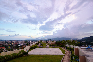 A scenic rooftop garden at sunset with a view of a city skyline and distant mountains under a cloudy sky.