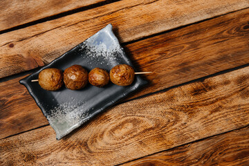 Shish kebab made from small young round grilled potatoes with a baked skin on a brown wooden background.