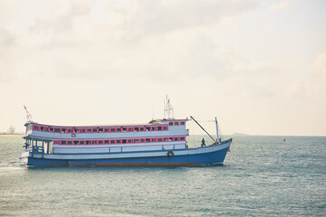 Fototapeta premium Scenic View of Thai Tour Boat on Tropical Ocean Water with Lush Hills Beyond